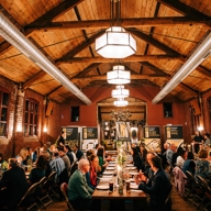 Interior of a venue with a dinner, long tables with guests sitting either side and stage at far end. 