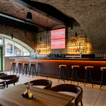 The bar at Tavern on The Quays, with the vaulted stone ceiling plus bar stools lined up along the bar and tables and chairs in the foreground.