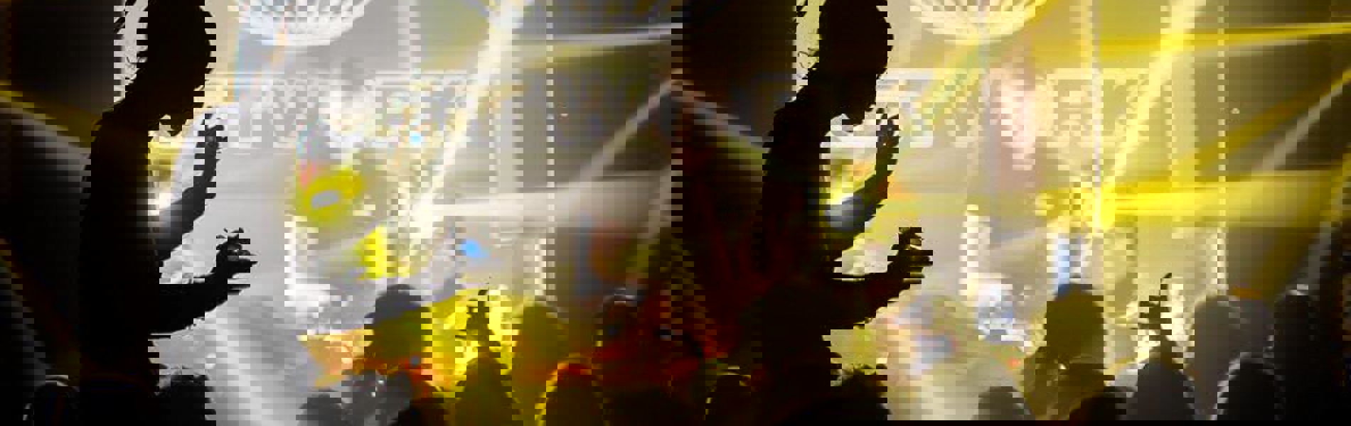 A nightclub full of people dancing, lit by yellow lighting.