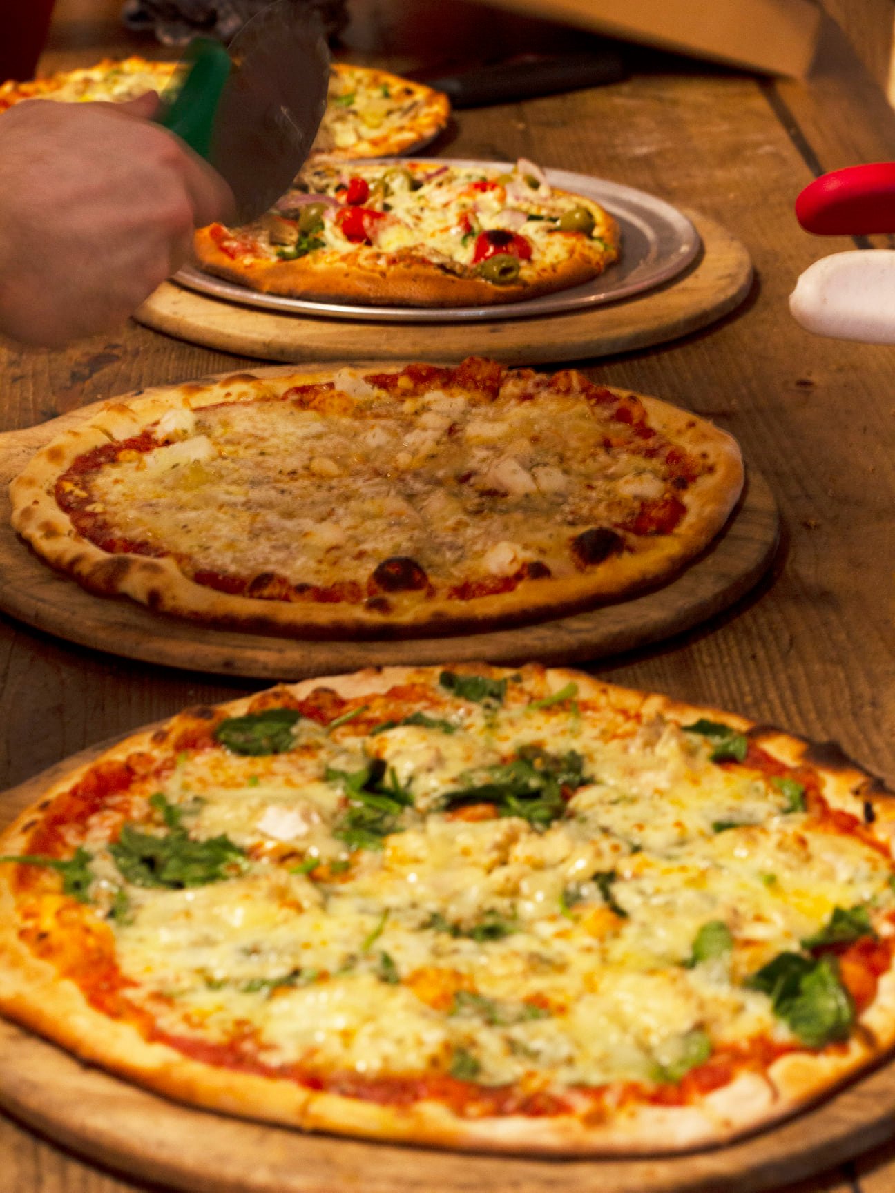 Pizzas fresh out the oven about to be cut up into slices.