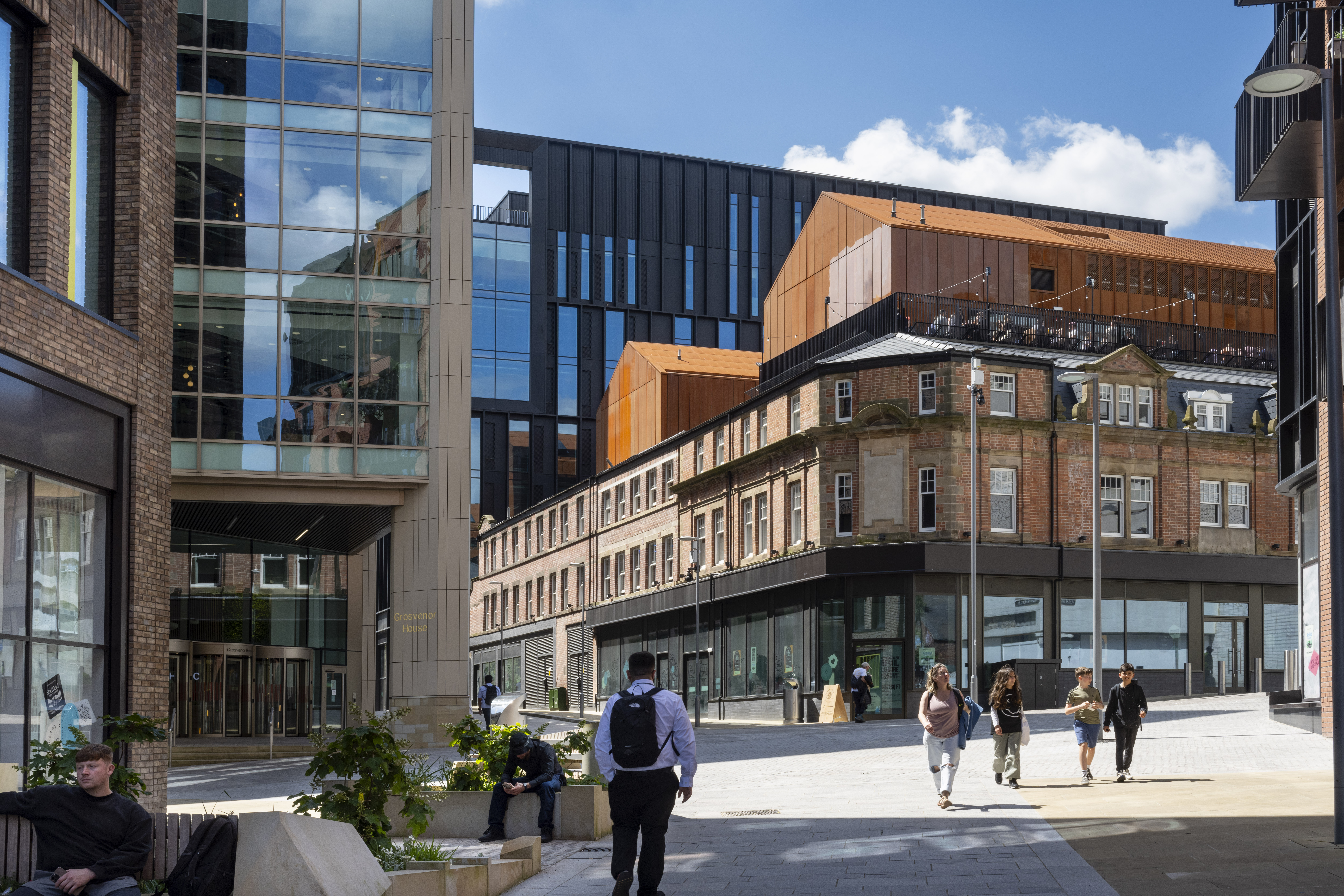 People walking in the sunshine in a pedestrian area that leads up to the food hall Cambridge Street Collective.