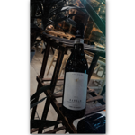 A bottle of 2014 Barolo wine labeled "Vinum Vita Est" and "Terre del Barolo" displayed on a wooden rack. The background features chairs and tables in an indoor dining setting, suggesting a restaurant atmosphere.