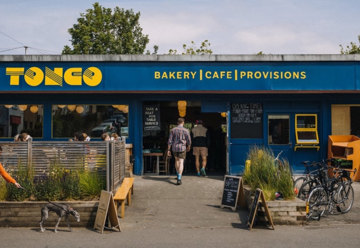 The exterior of a building painted blue. There is yellow lettering above the window and door that reads ' Tonco' and 'Bakery, Cafe, Provisions'.
