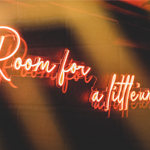 Red neon sign on a wall at Nook that reads 'Room for a little'un'
