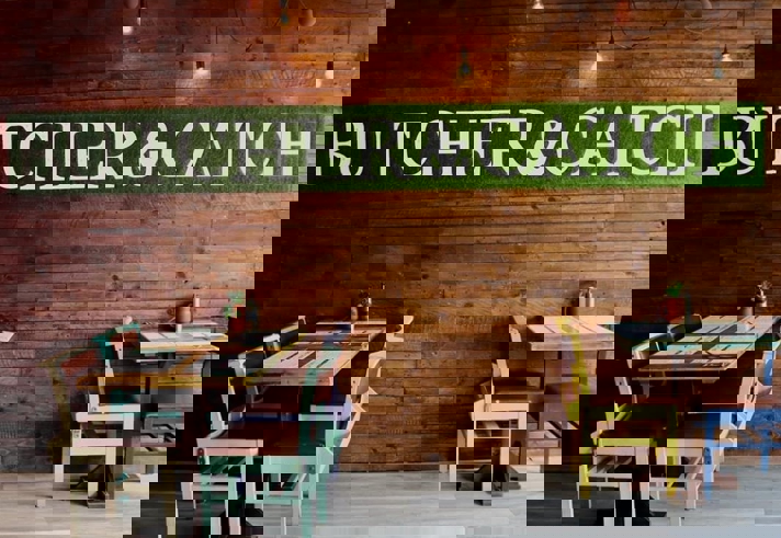 Restaurant tables next to a naked brick wall with a green sign that reads 'Butcher & Catch'.
