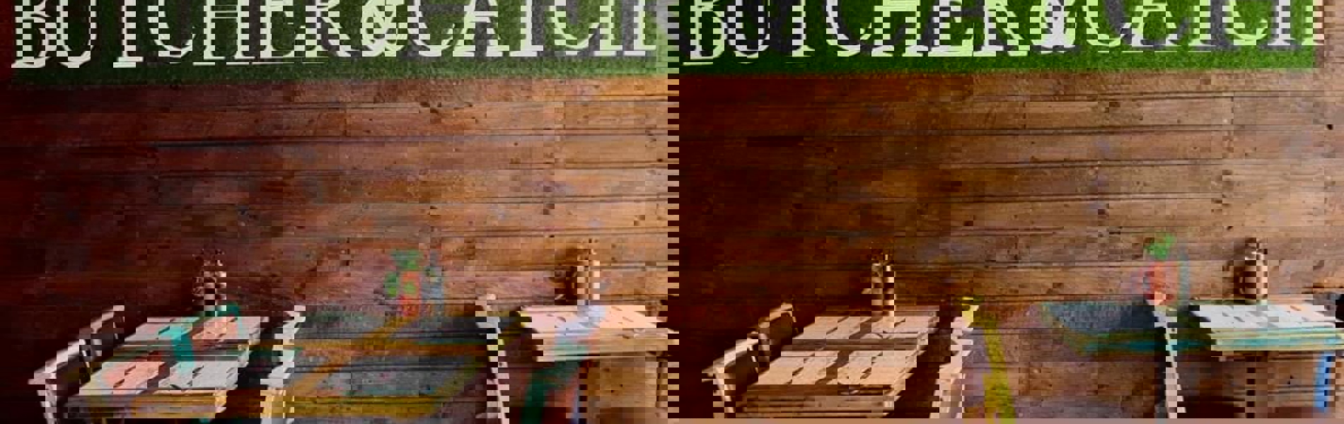 Restaurant tables next to a naked brick wall with a green sign that reads 'Butcher & Catch'.
