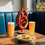 Two glasses of beer and warm pretzels on a table next to a window.